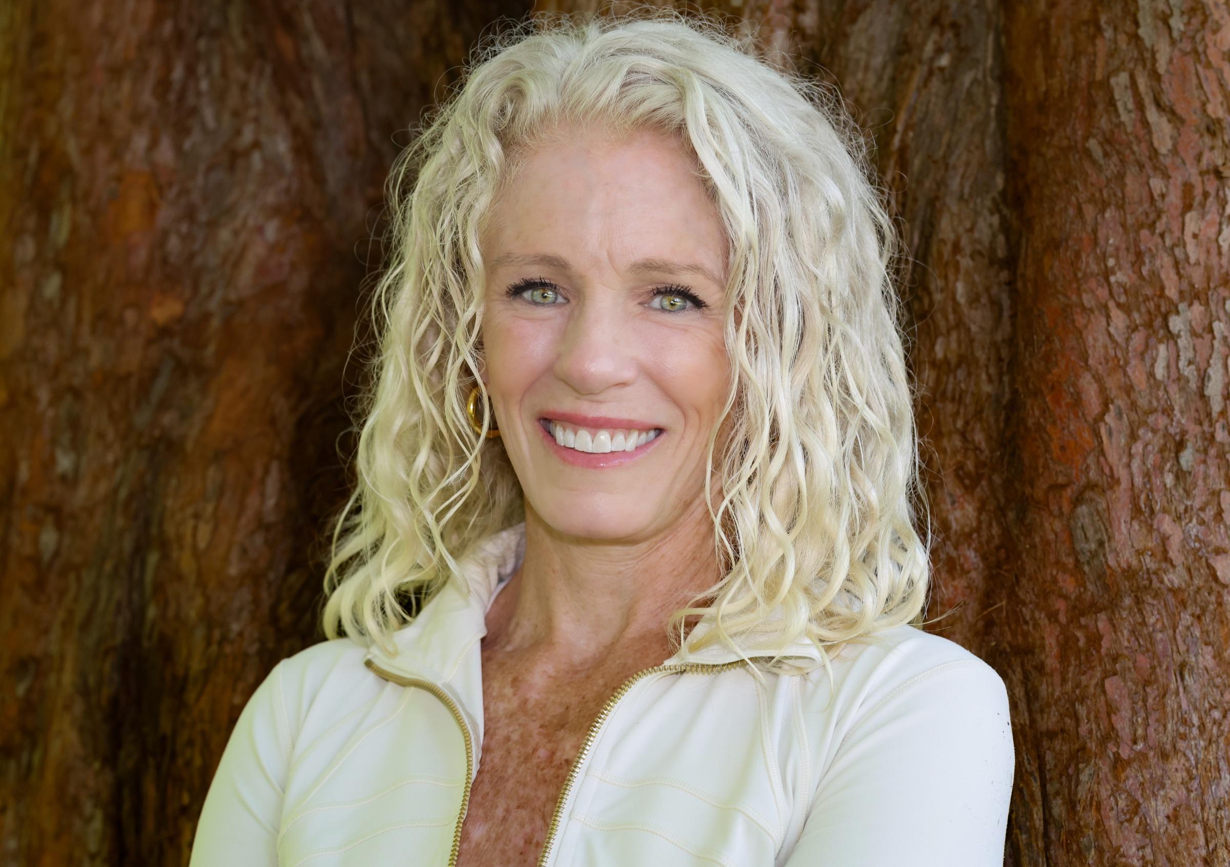 Close portrait of Stephanie Colwell in front of a cedar trunk, smiling