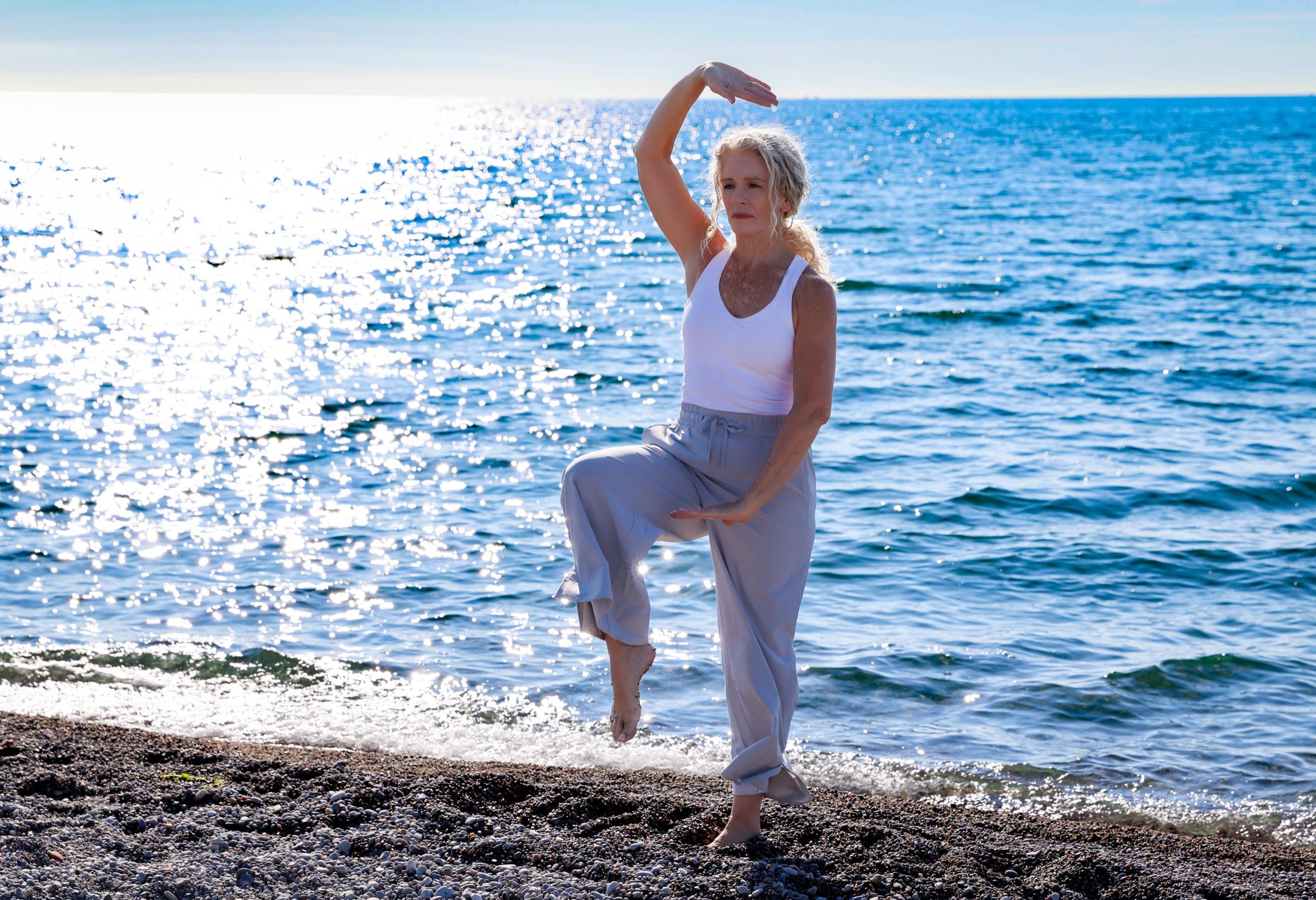 Stephanie balancing on one leg in a crane pose at the water's edge