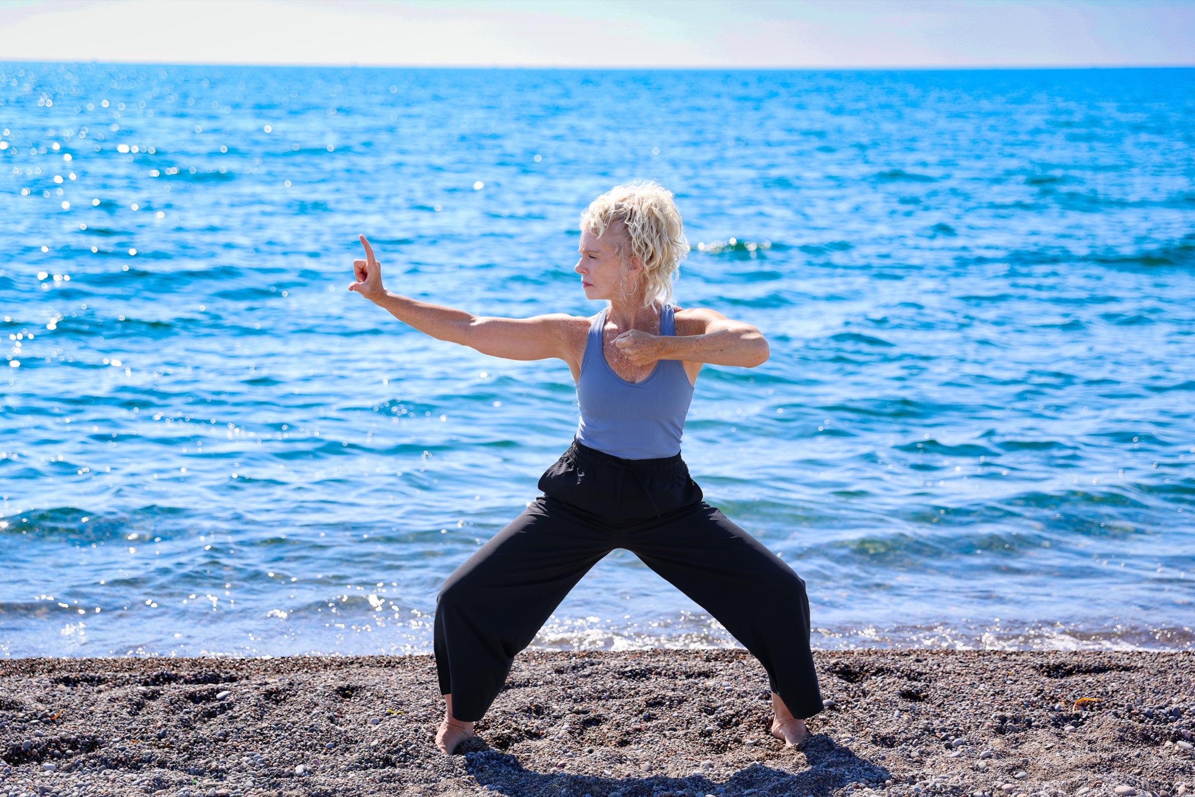Stephanie extending one arm in a long archer form, gaze following her hand over the water